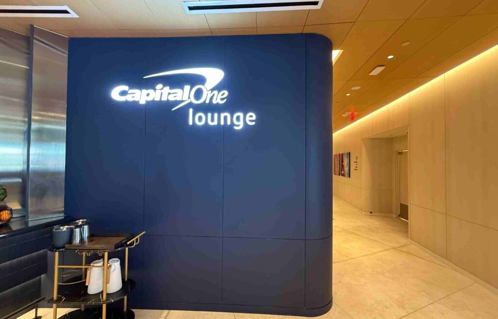 Blue Capital One Lounge wall with illuminated logo and hallway entrance.
