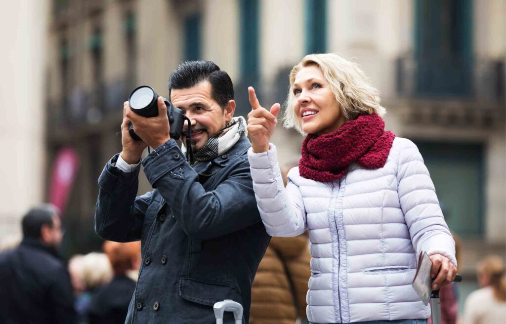 A happy retired couple exploring a city as the man takes photos with his camera, symbolizing retirement migration.