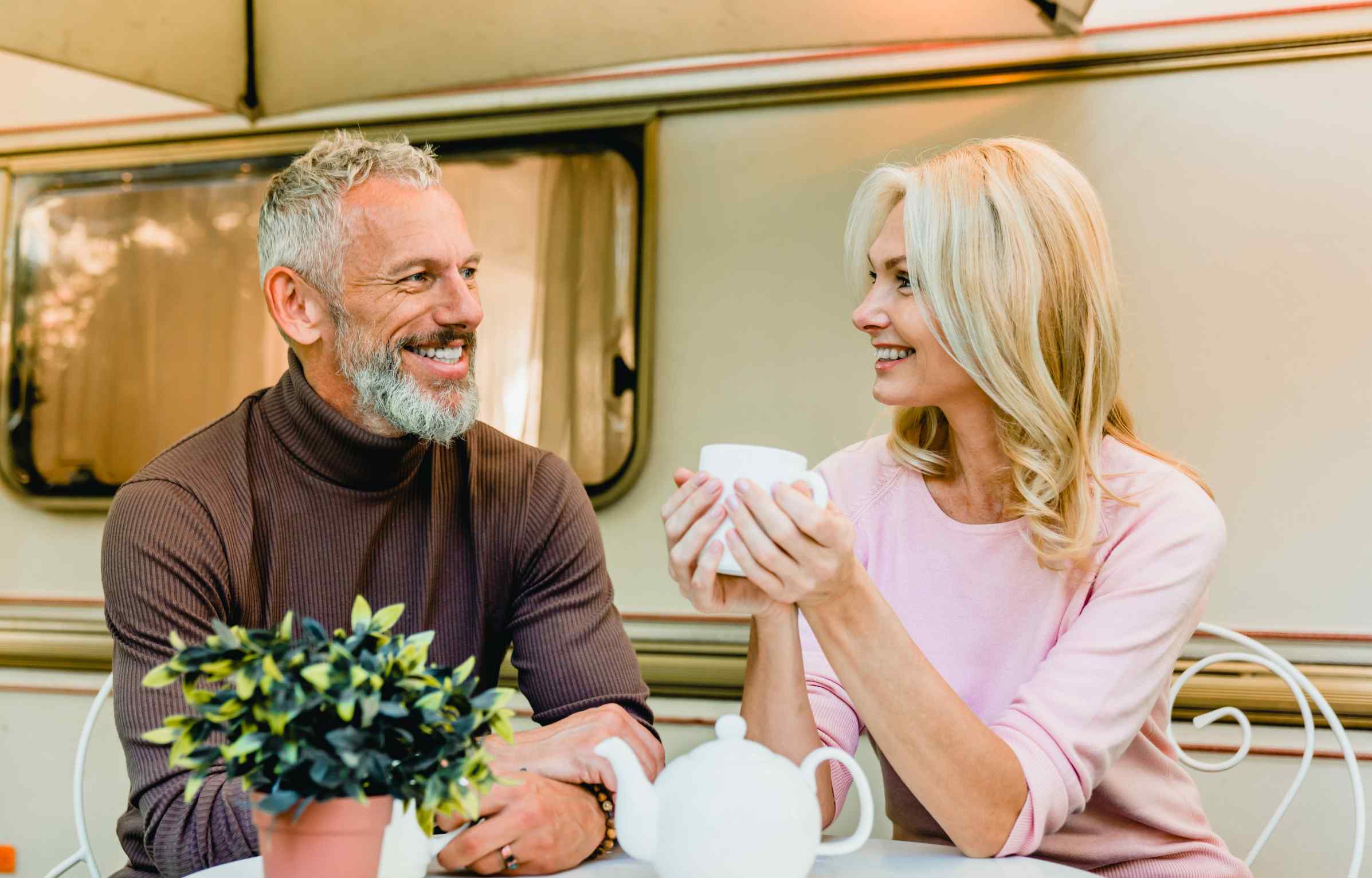 A happy mature couple enjoys tea outdoors in Europe, smiling and relaxed while sharing a peaceful moment together.