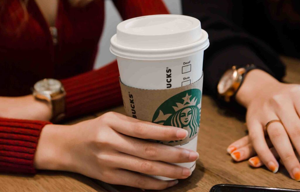 A customer sitting at a table holding a Starbucks coffee cup, representing everyday participation in the Starbucks Rewards program and brand loyalty.