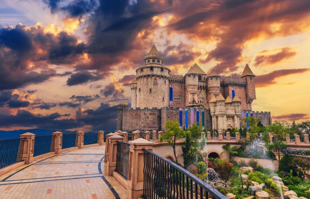 A large castle-like structure in Da Nang, Vietnam, set against dramatic sunset clouds with landscaped gardens in front.