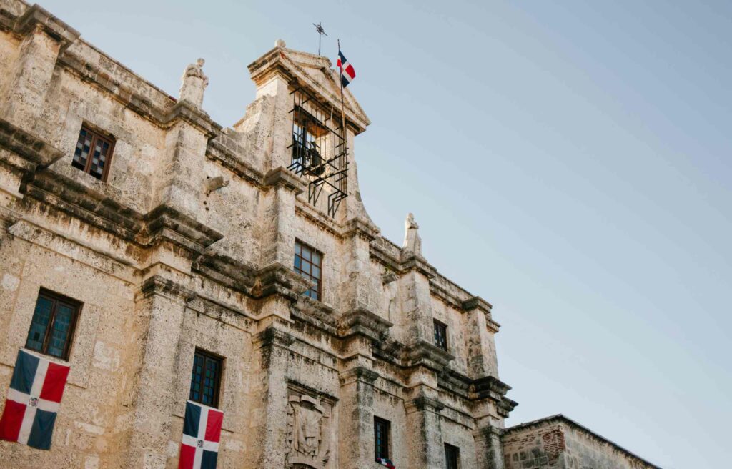 Historic stone building in the Dominican Republic displaying national flags on its facade.