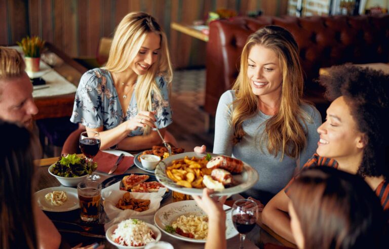A group of people enjoying dinner together, passing dishes and smiling around a full table.