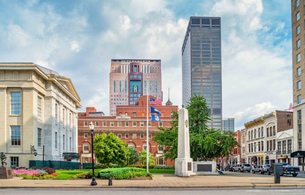 Louisville, Kentucky with historic and modern buildings, a city square, and flags waving under partly cloudy skies.