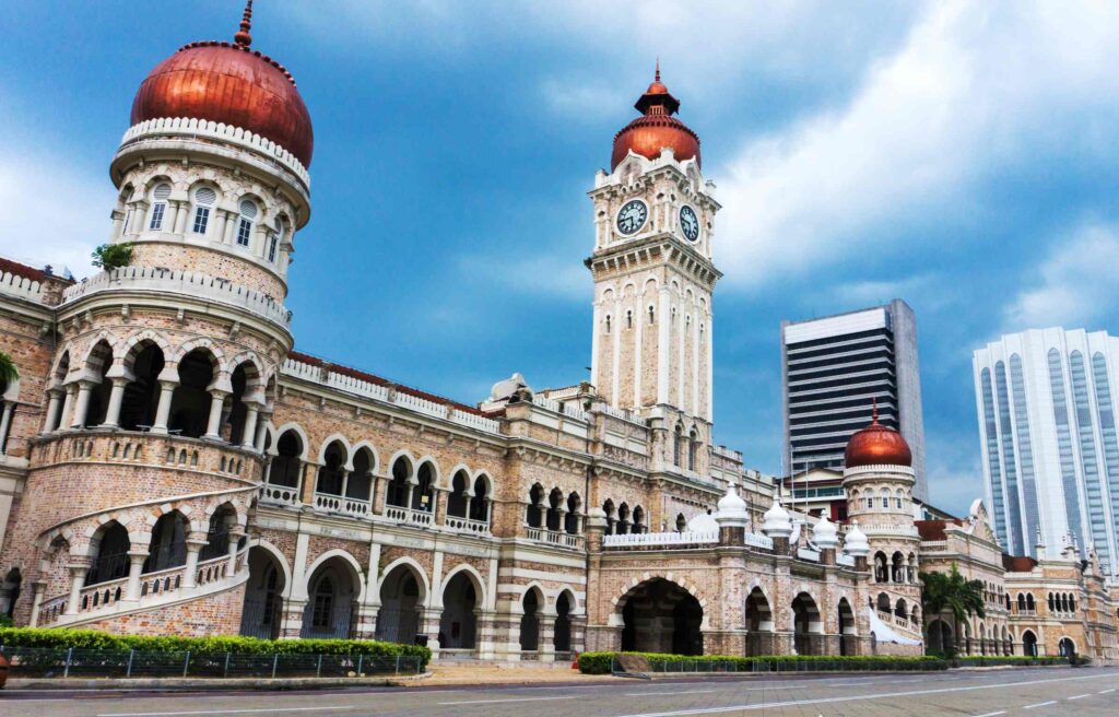Historic Sultan Abdul Samad Building in Kuala Lumpur with ornate arches, clock tower, and modern city skyline in the background.