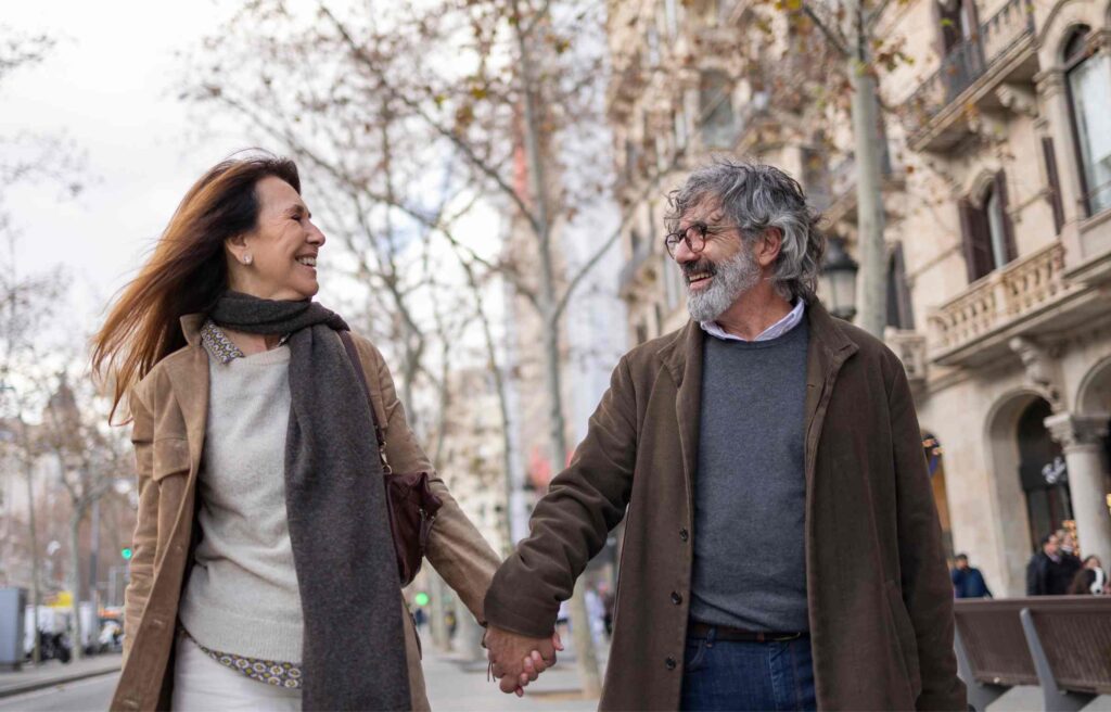 A smiling mature couple walks hand in hand through a European city street, enjoying the future of retirement abroad with confidence and ease.