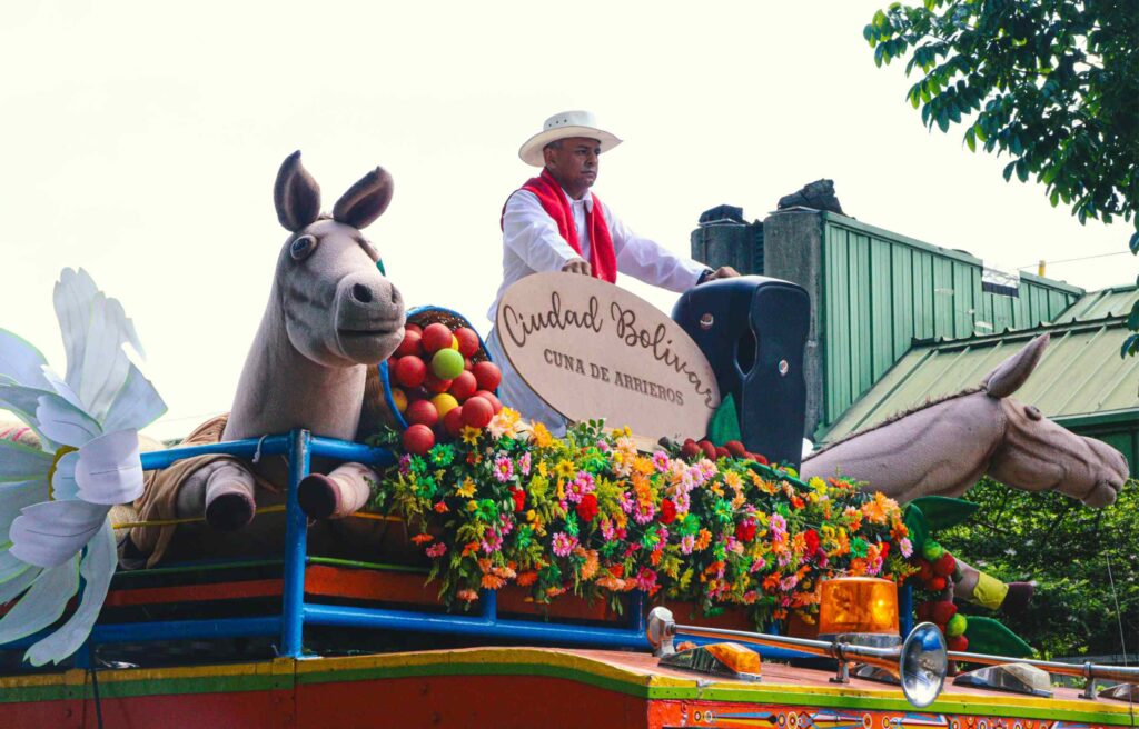 A man in traditional clothing rides a decorated parade float with flowers and horse figures in Medellín, Colombia, a city now recognized among digital nomad hotspots.
