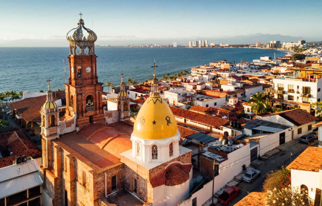 Aerial view of Puerto Vallarta with its historic church, red tile rooftops, and coastline along the Pacific Ocean.