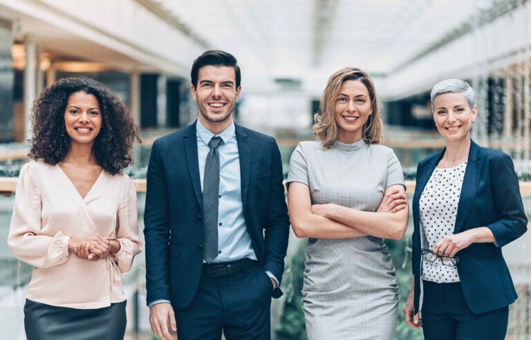 A group of four professionals standing together and smiling in a bright modern office space.