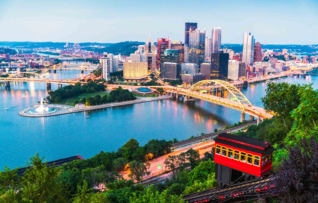 Evening view of downtown Pittsburgh, Pennsylvania with the Duquesne Incline, golden bridges, and rivers reflecting city lights.