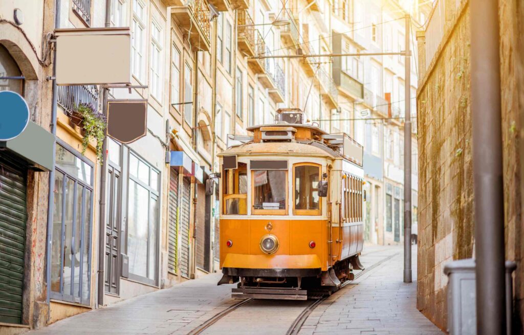 Historic yellow tram traveling through a narrow street lined with old buildings in Portugal, a popular destination offering affordable healthcare for retirees.