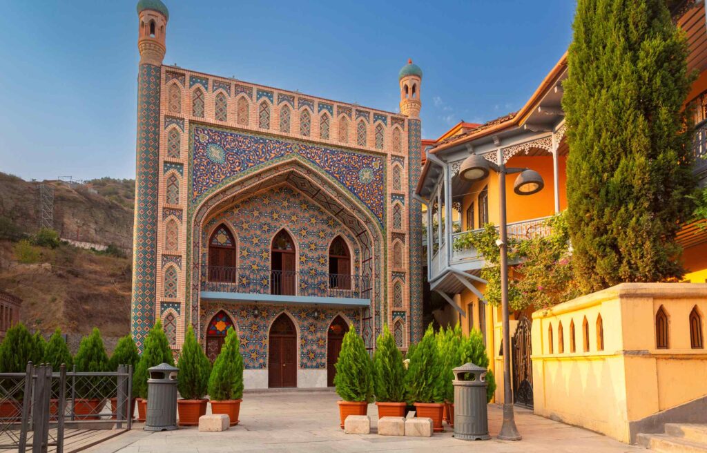 A beautifully tiled Persian-style building in Tbilisi, Georgia, standing beside colorful traditional wooden balconies.