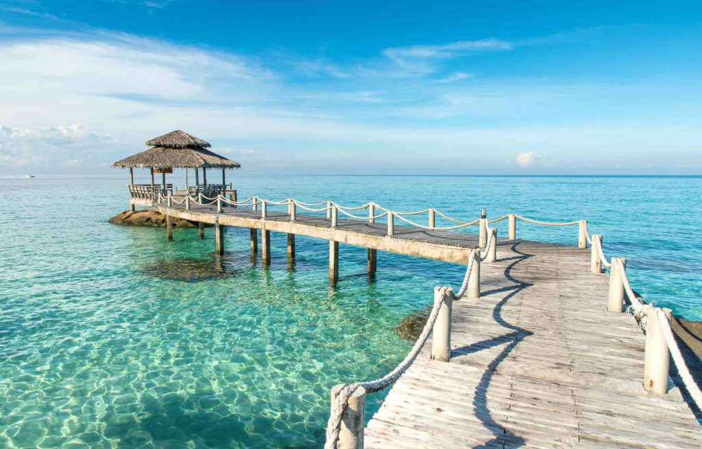 Wooden pier leading to a thatched pavilion over clear turquoise water in Thailand.