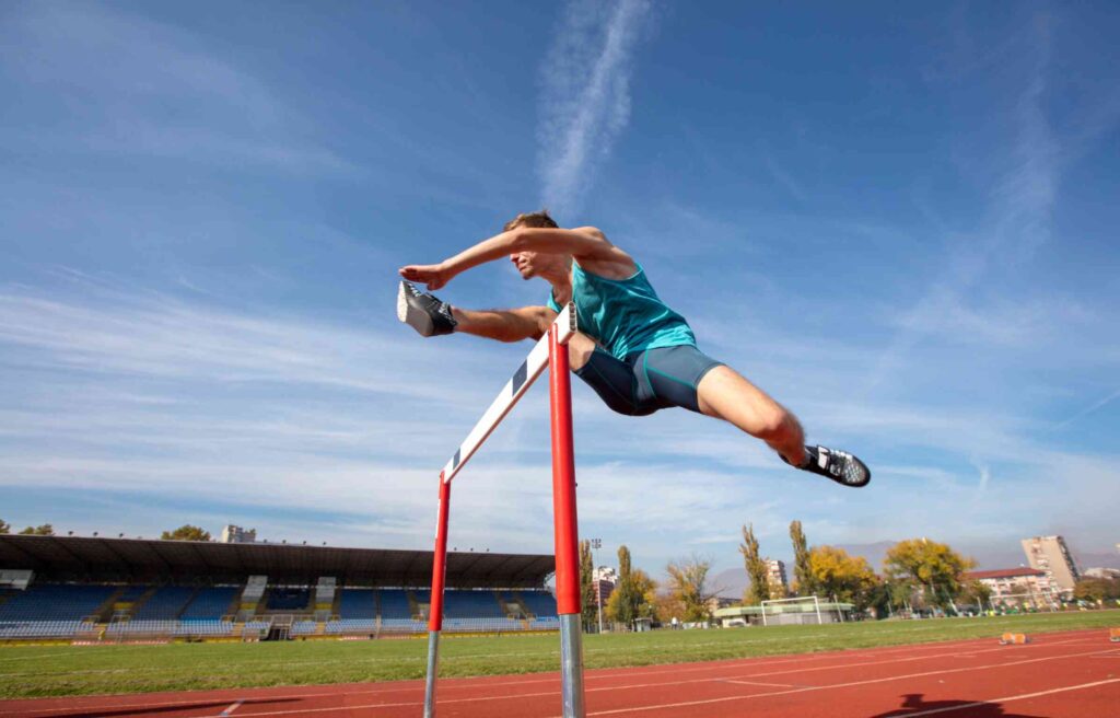 Track athlete jumping over a hurdle on a running track.