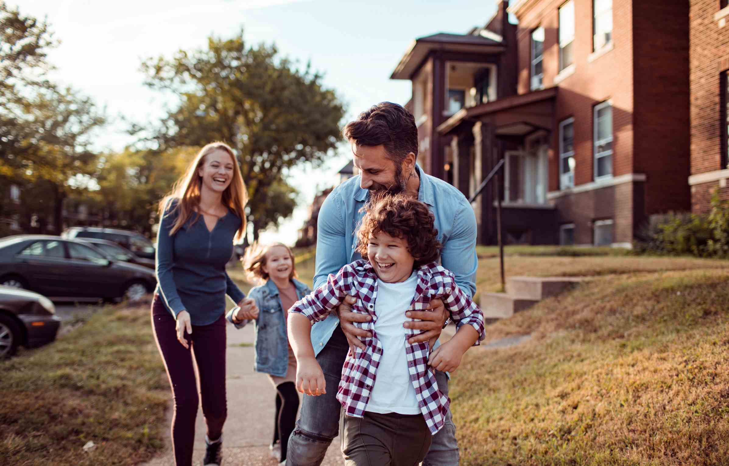 Young family playing and laughing together on a sidewalk in a suburban neighborhood.