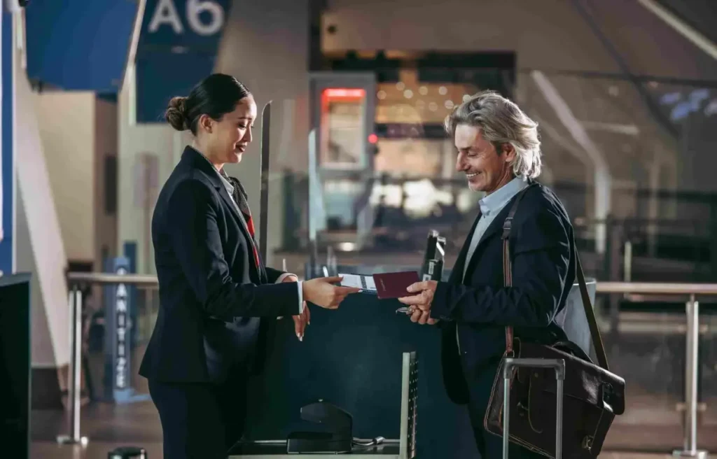 A male traveler hands his passport and boarding pass to an airline staff member at an airport check-in counter.