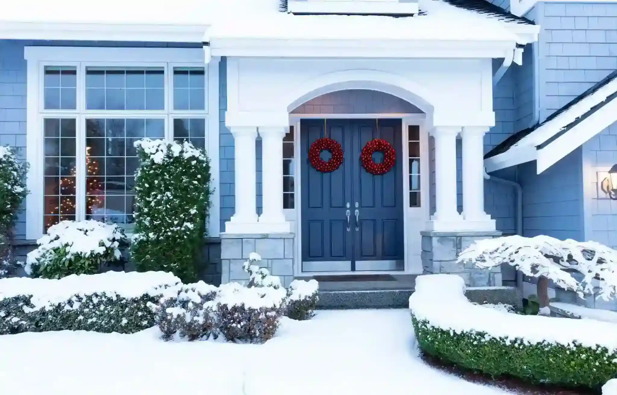 Snow covered home exterior with wreaths showing winter curb appeal during December home selling season.
