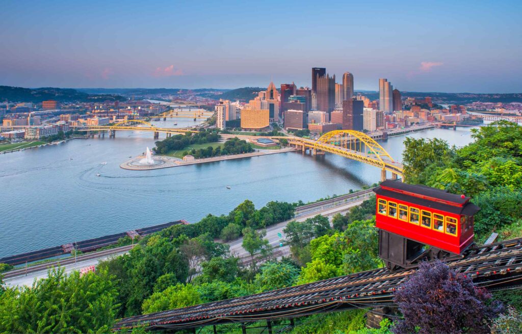 Pittsburgh skyline overlooking the rivers and yellow bridges with an incline railway car in the foreground.