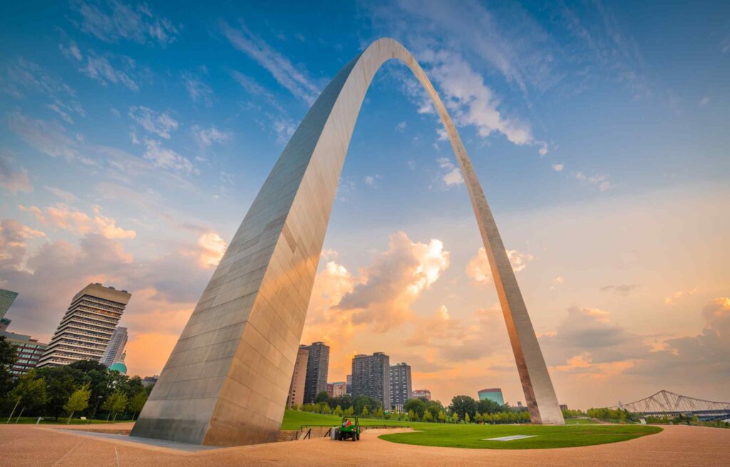 The Gateway Arch towering over downtown St. Louis during a colorful sunset.