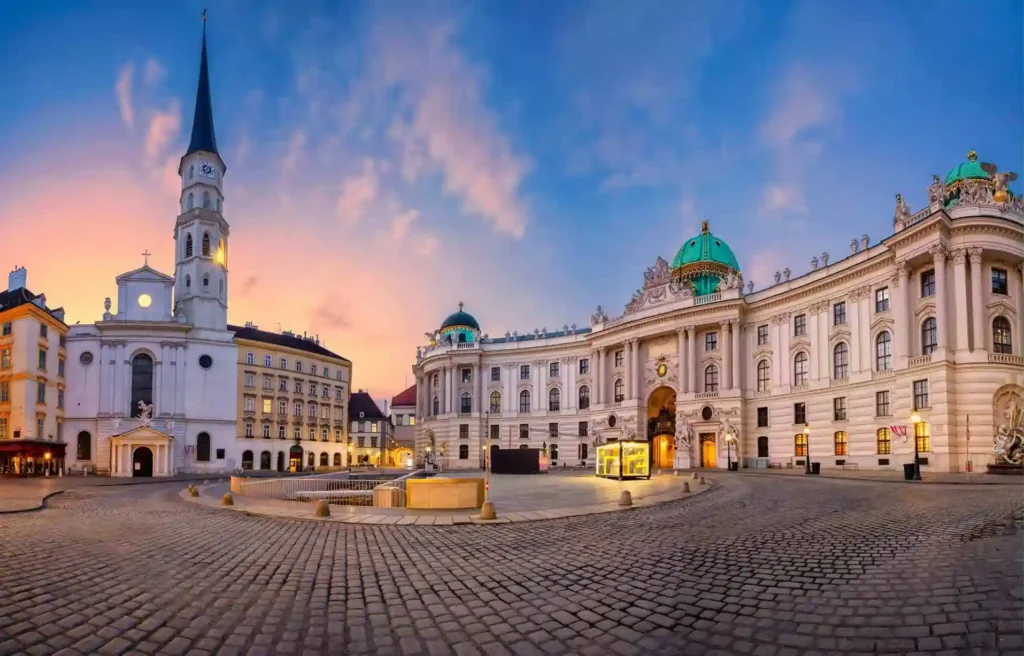 Historic Vienna city center at sunset with Hofburg Palace, cobblestone square, and illuminated buildings in Austria.