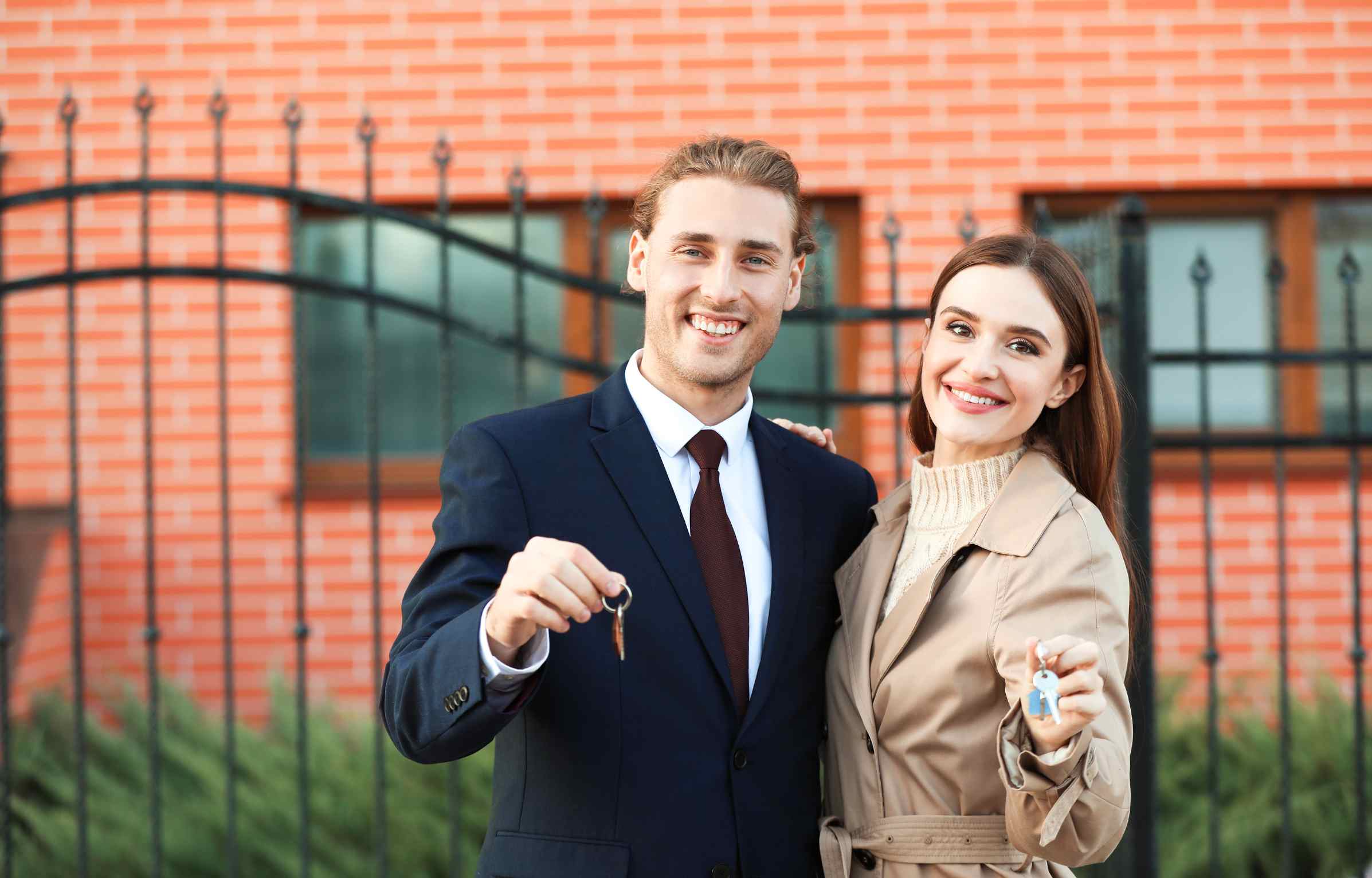 Young couple smiling while holding house keys outside their new home.
