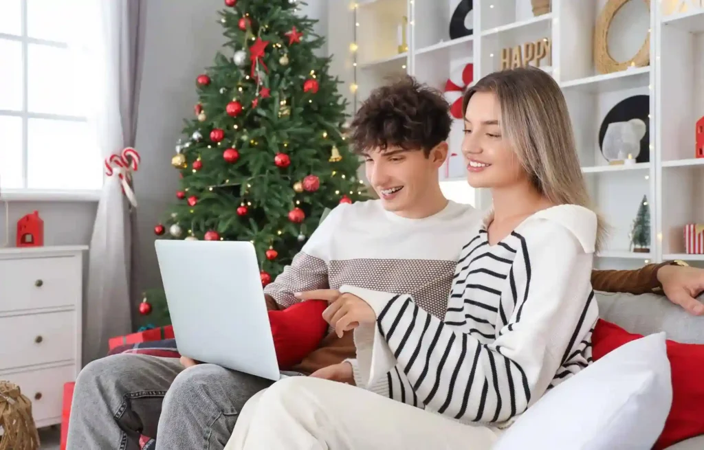 Young couple using a laptop together while relaxing at home near a christmas tree.