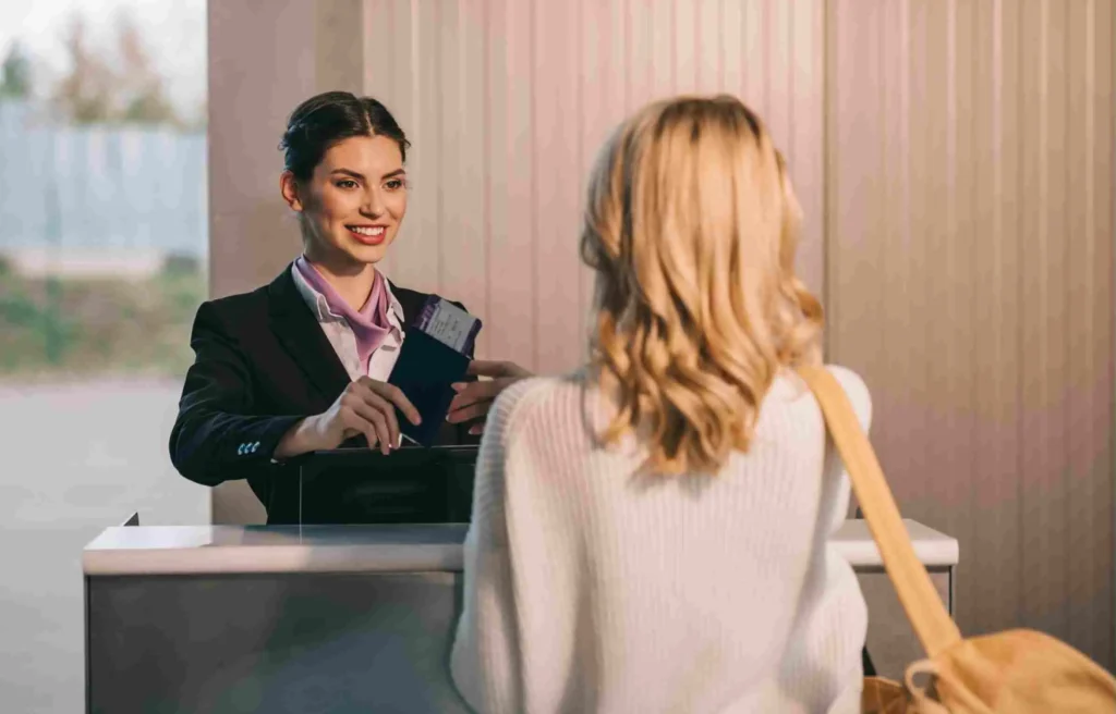 An airport check-in agent smiles while handing a passport and southwest boarding pass to a female traveler at the counter.