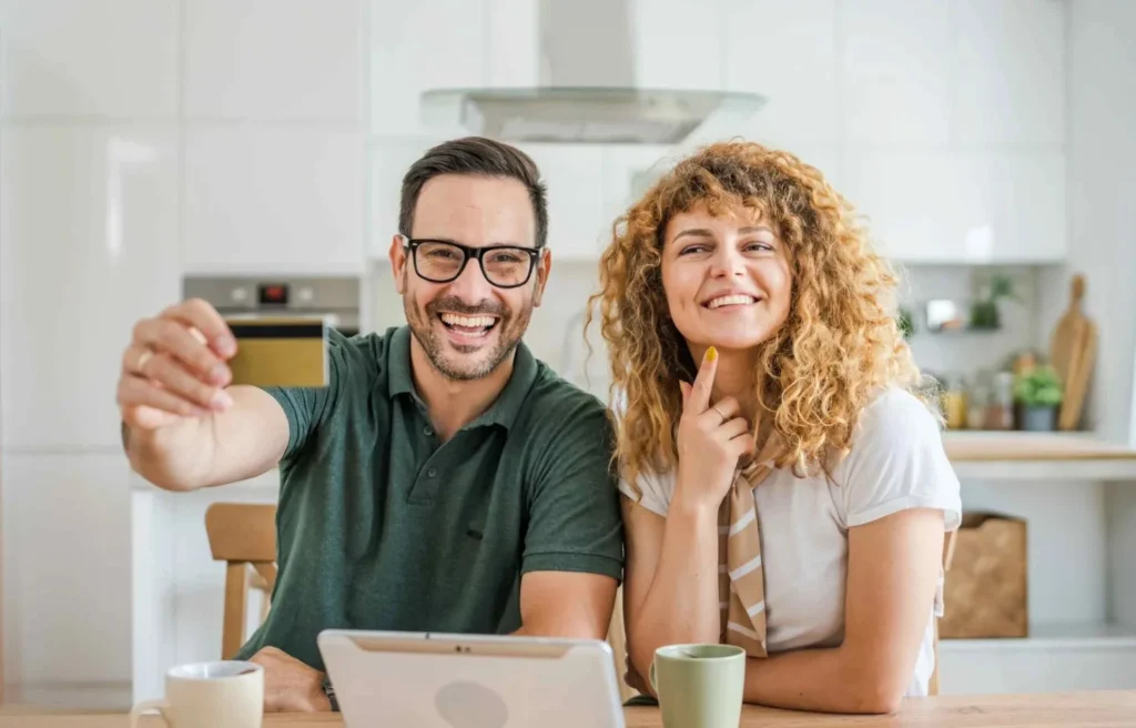 Couple at kitchen table reviewing finances while holding a credit card and tablet.