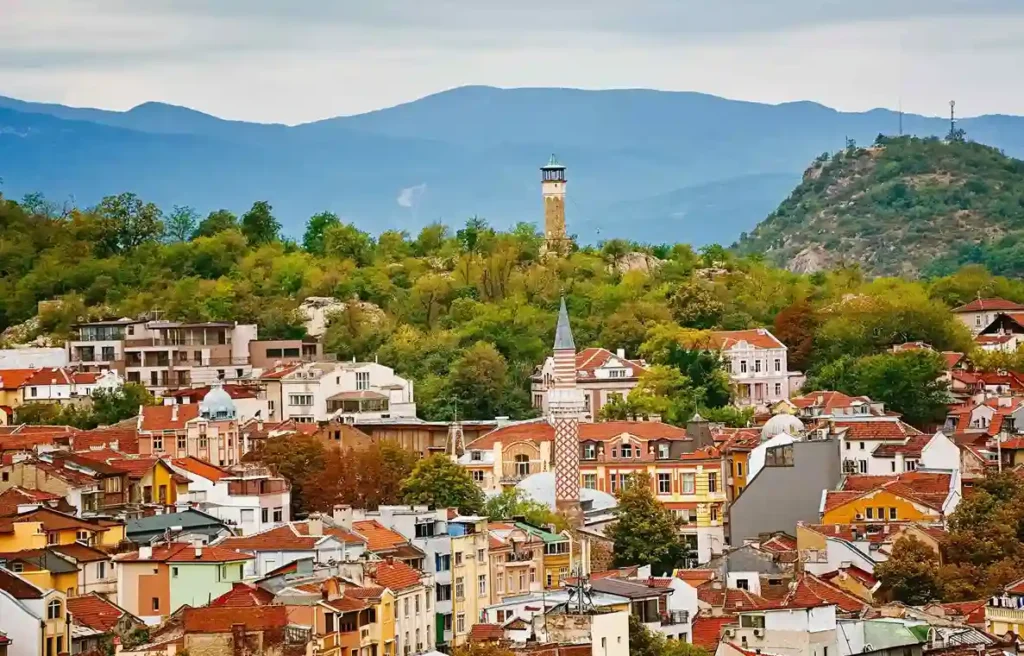 Historic Bulgarian cityscape with red rooftops, green hills, and mountains illustrating everyday life in Bulgaria.