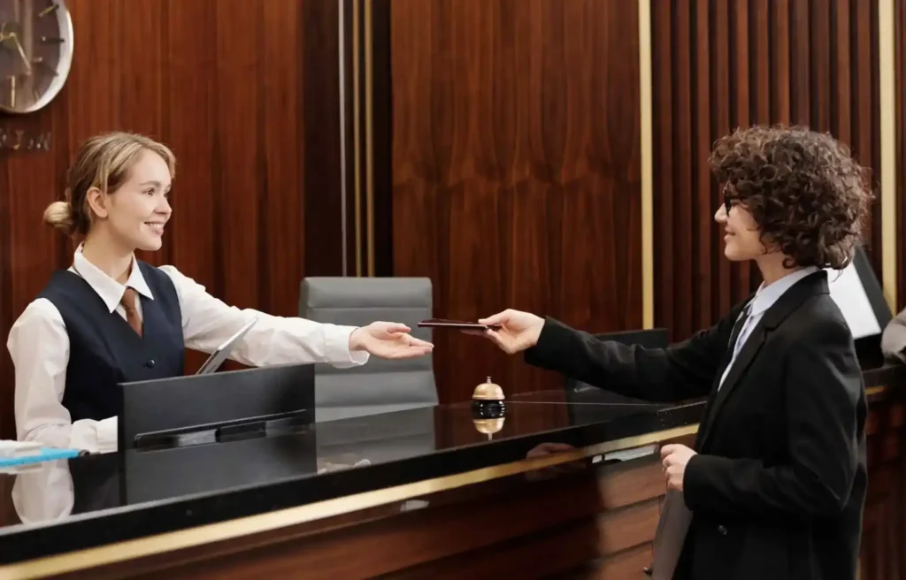 Hotel receptionist hands a room key to a guest at a front desk, completing check-in at a modern hotel lobby