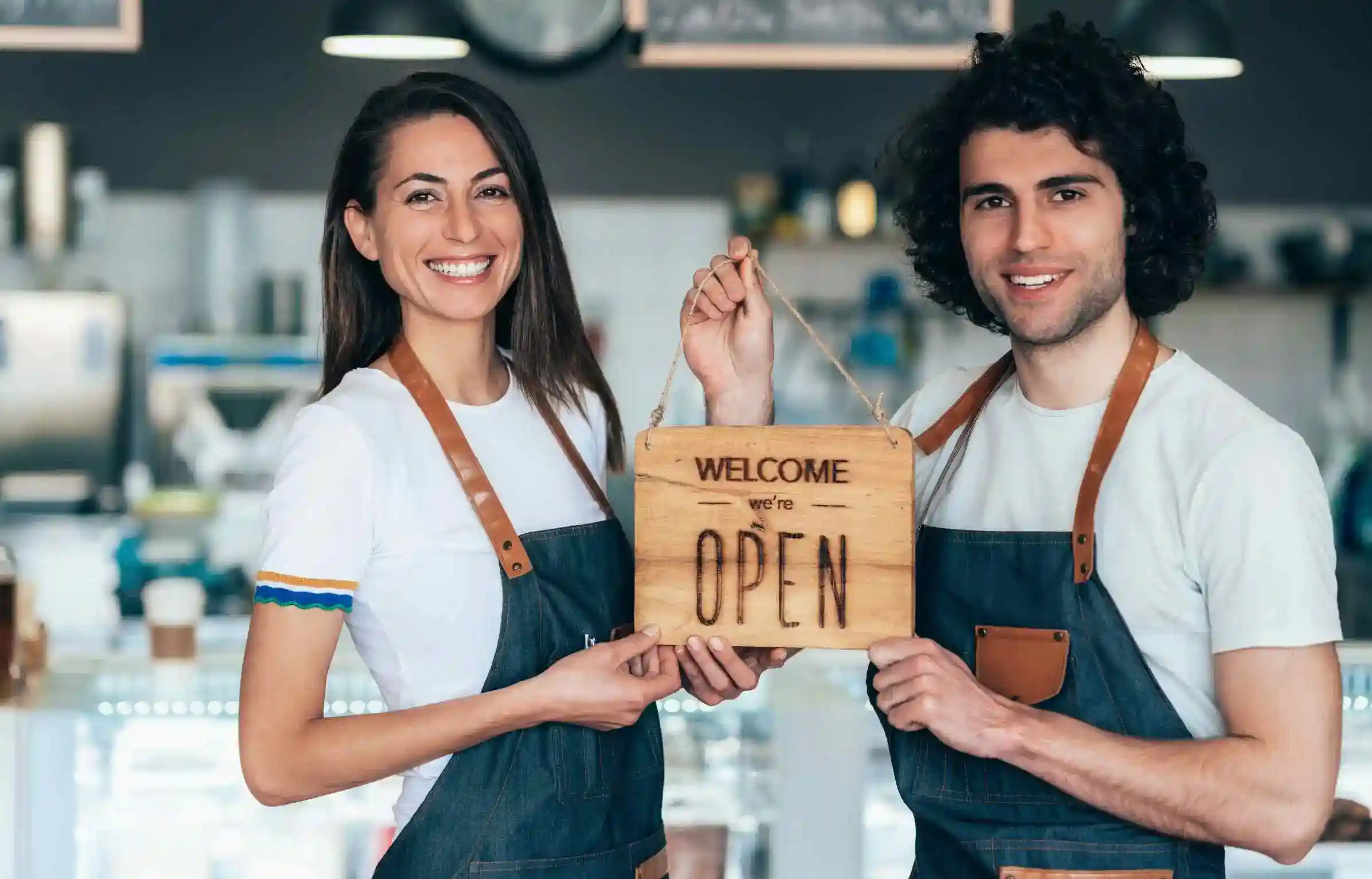 Two café owners holding an open sign and smiling behind the counter.