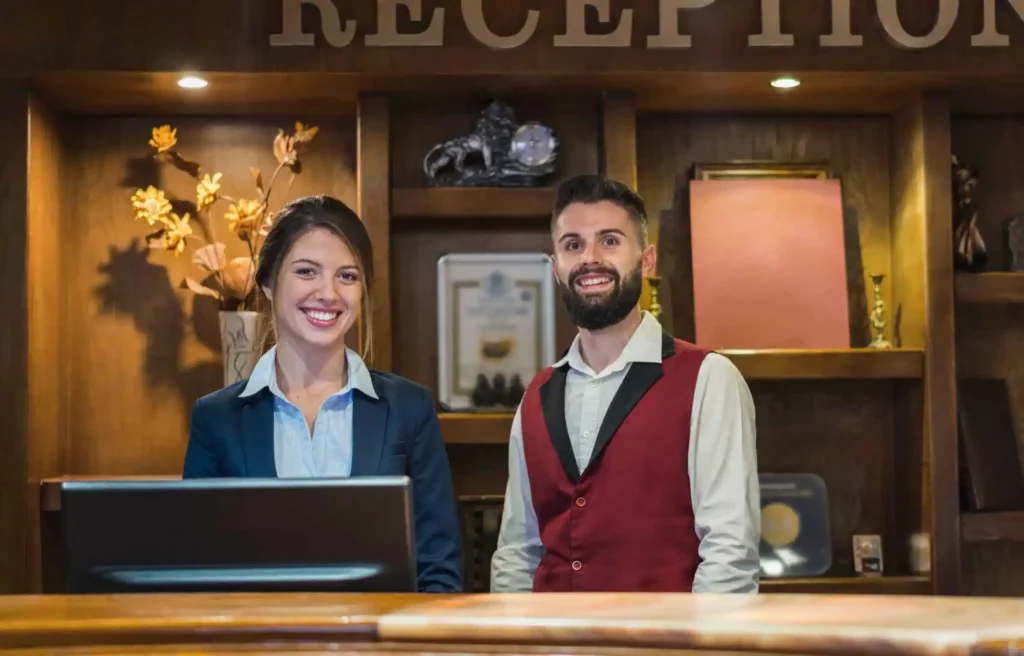 Hotel reception staff smiling behind front desk in a modern lobby.