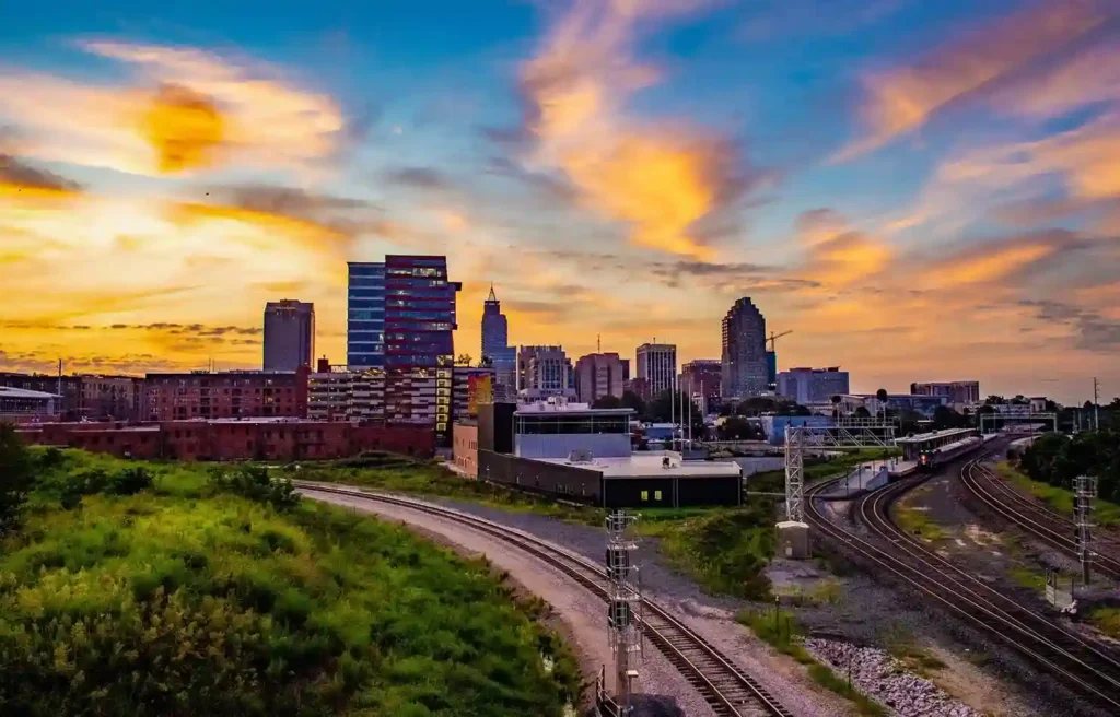 Raleigh skyline at sunset with rail lines, representing the Research Triangle innovation corridor.