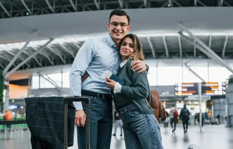 Young couple at airport terminal holding boarding pass and luggage before departure.