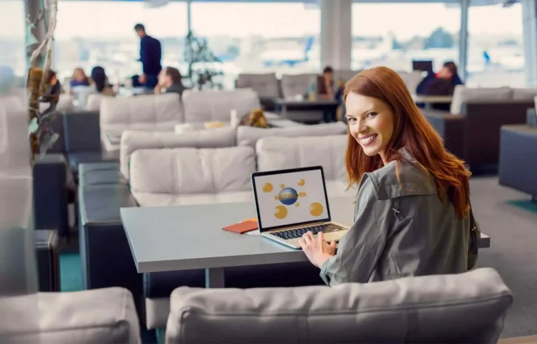 Business traveler working on laptop inside airport lounge seating area with passengers relaxing in background.