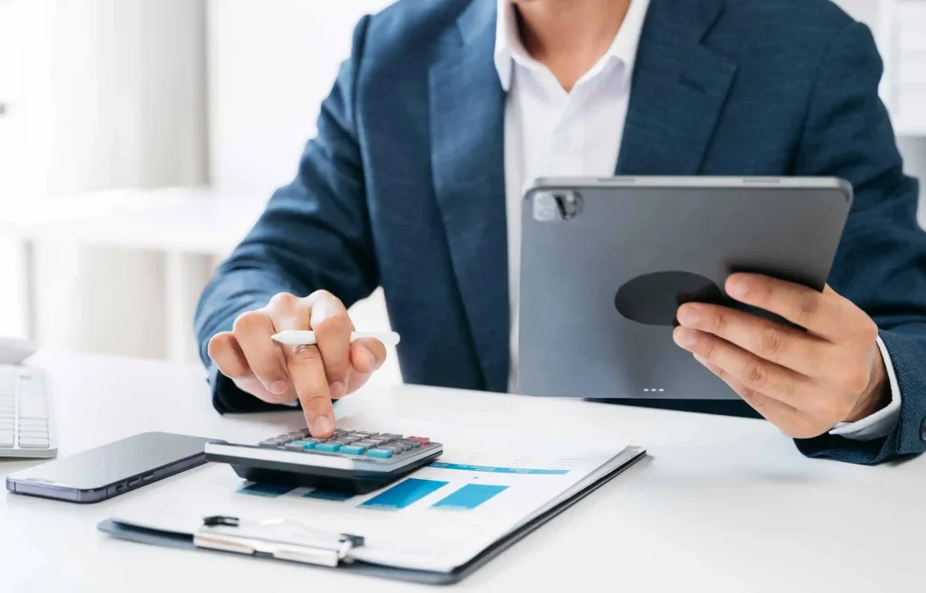Business executive using tablet and calculator to estimate how much does corporate housing cost.