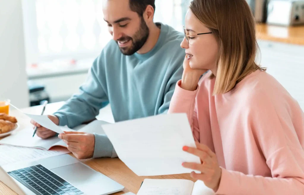Couple reviewing financial papers and learning how to create your own retirement plan at home with laptop and documents.