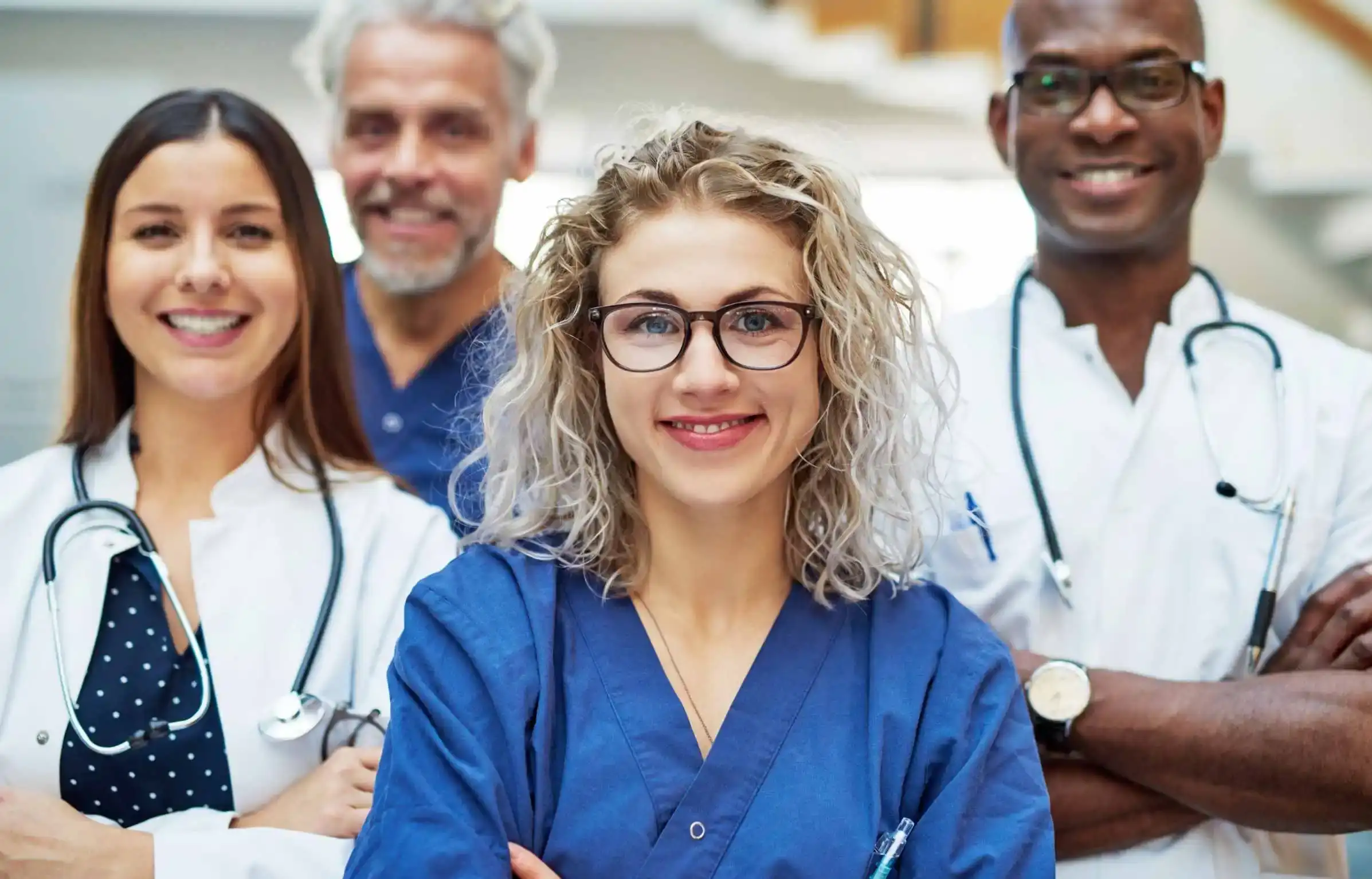 Diverse healthcare professionals smiling together in hospital setting with stethoscopes.