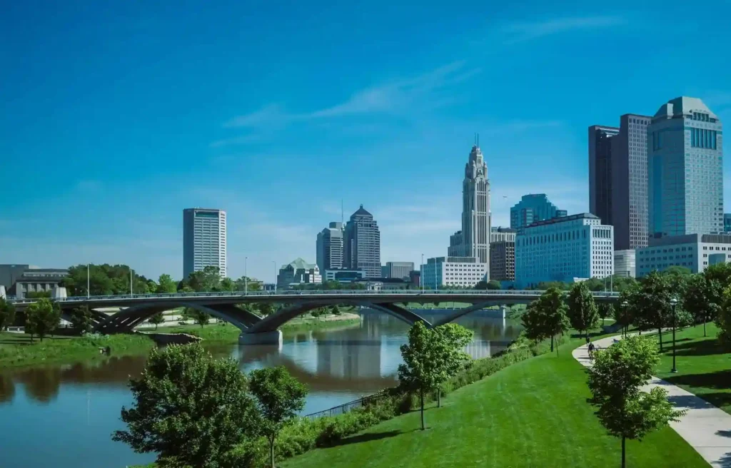 Ohio Columbus skyline with riverfront park, bridge crossing the river, and green walking paths.