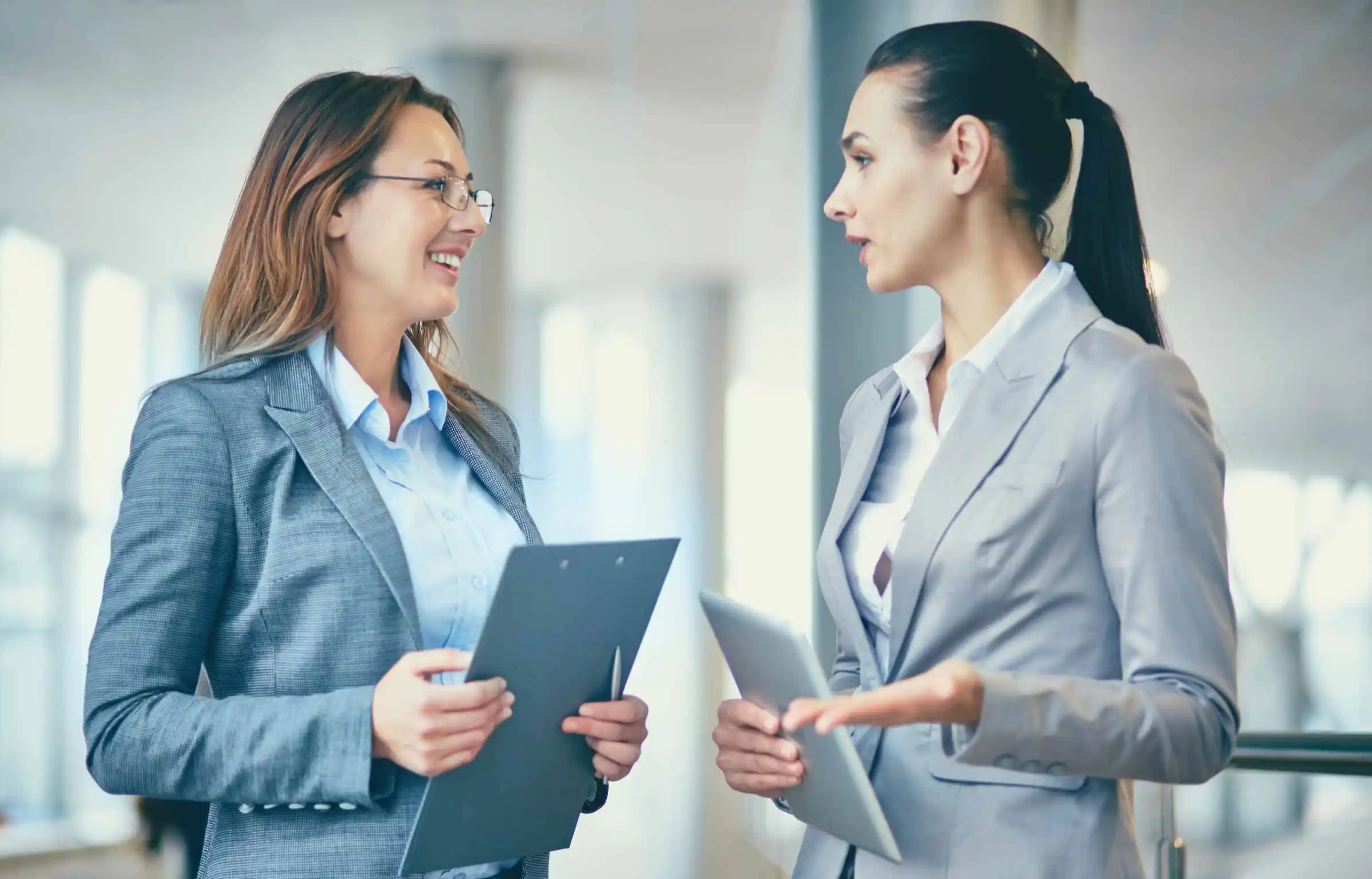 Professional women discussing relocation documents and employee mobility plans in a modern office corridor.