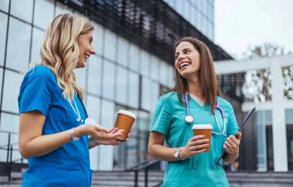 Two nurses in scrubs talking about healthcare employee relocation outside a modern hospital.