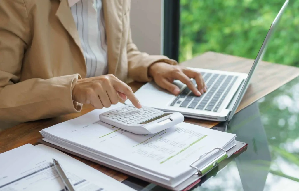 Woman calculating cost of relocating internationally budget with laptop and documents at home desk.