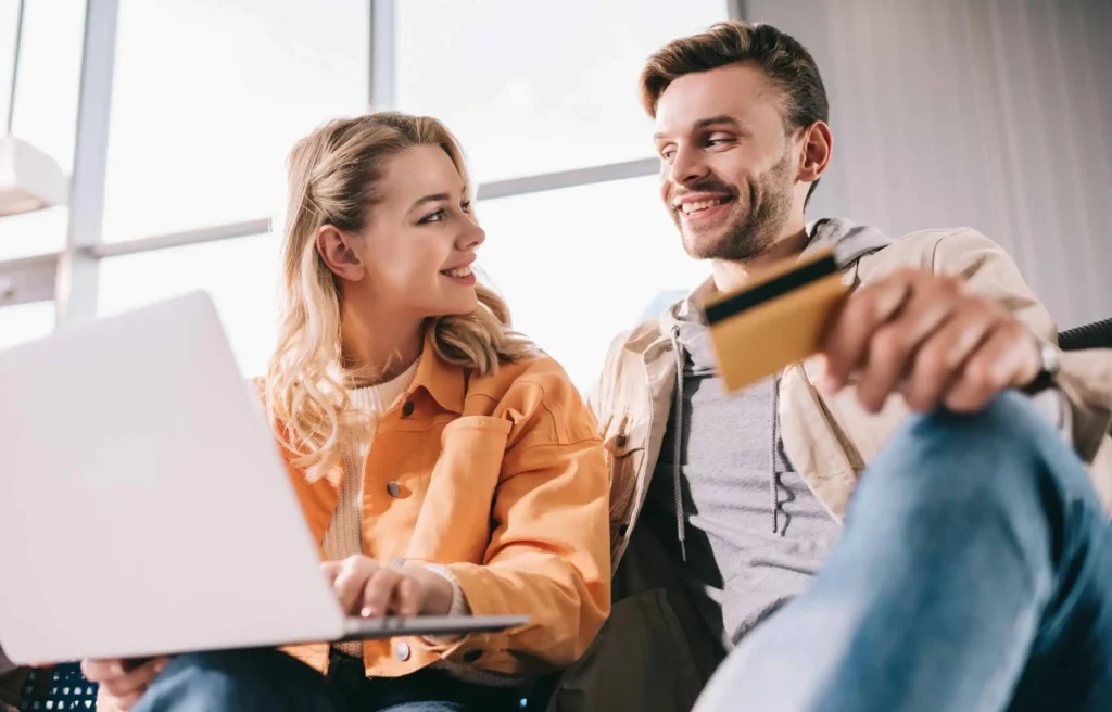 A couple using a laptop and a credit card at the airport, learning how to earn aa loyalty points quickly.