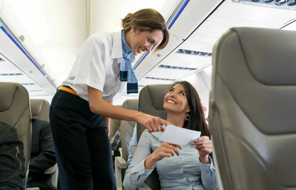 An American Airlines flight attendant is assisting a smiling passenger with a boarding pass in the cabin.