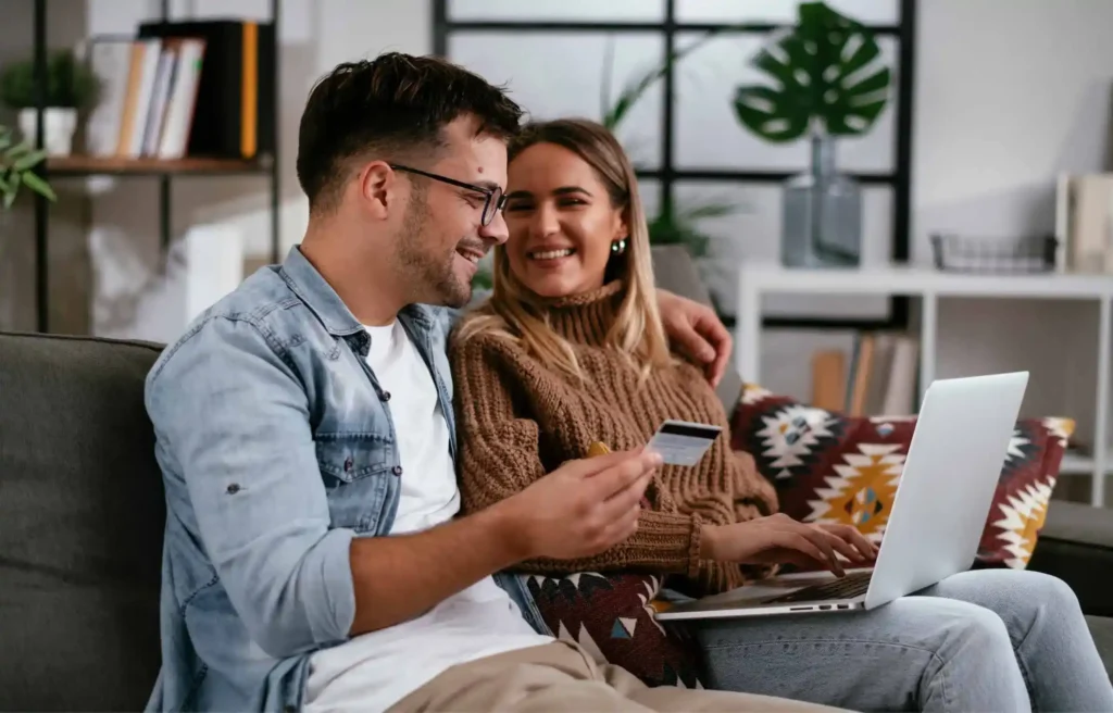 Couple using credit card and laptop at home to plan expenses and earn travel rewards during relocation.