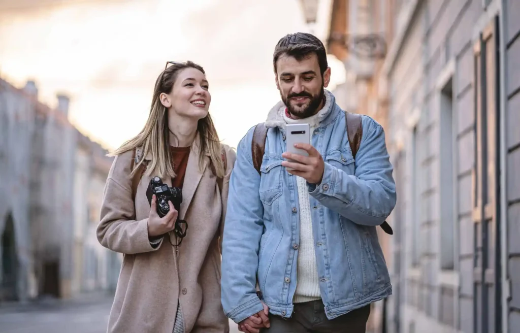 Couple walking in city checking phone while planning relocation and travel expenses.