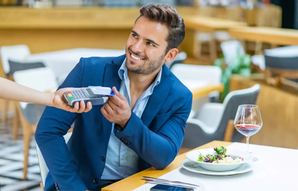 Customer paying with a credit card at a restaurant table, illustrating marriott bonvoy business american express card review.