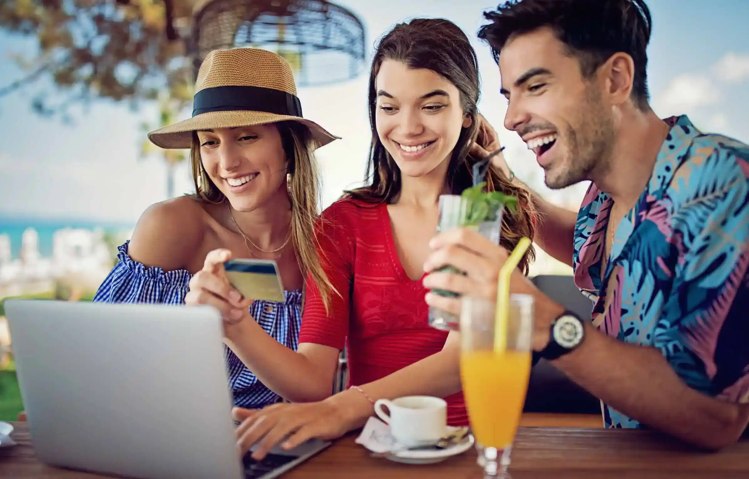 Friends are using a credit card and a laptop at a cafe while planning travel and earning rewards points.