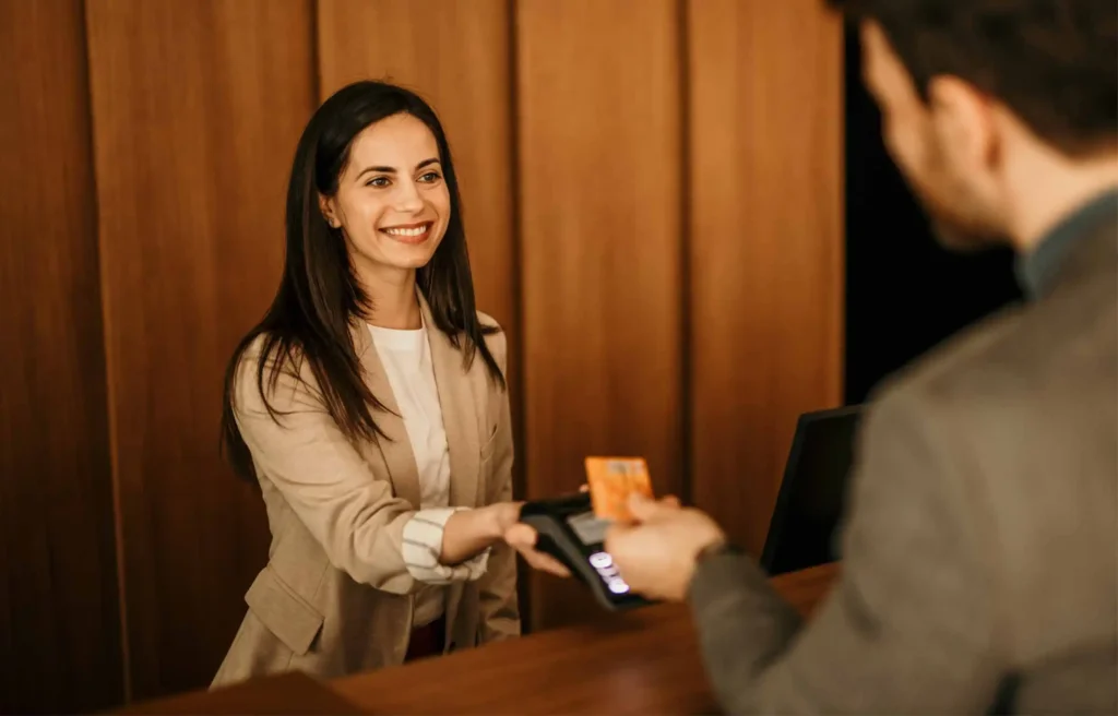Hotel receptionist processing card payment at the front desk during guest check-in.