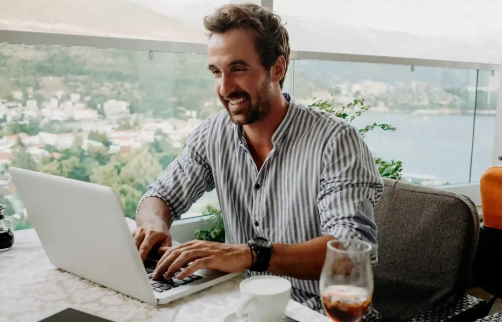 A man working remotely on a laptop with a scenic city view, representing high-paying digital nomad jobs.